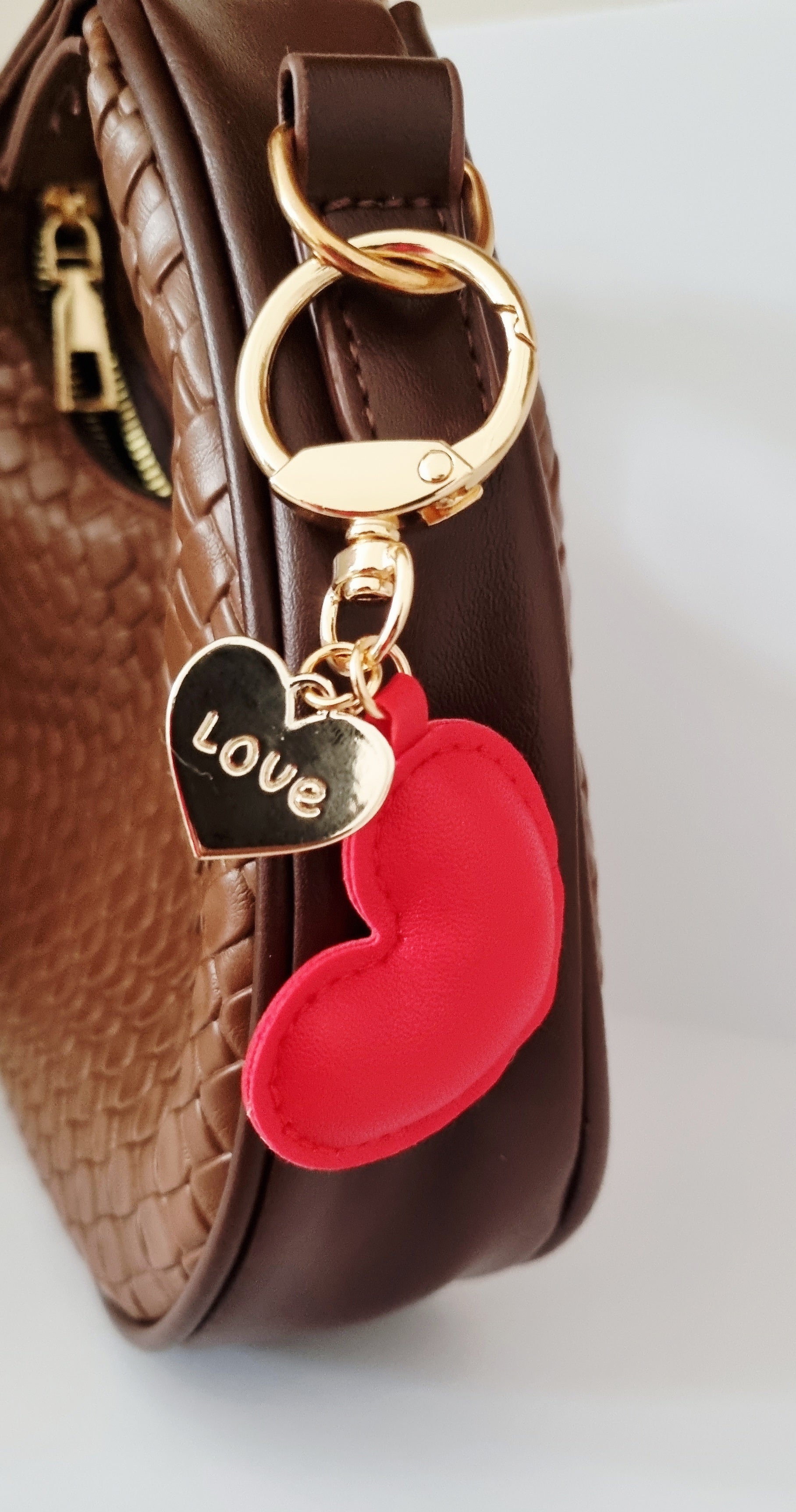 Heart-shaped keychain with 'LOVE' tag attached to a brown handbag.