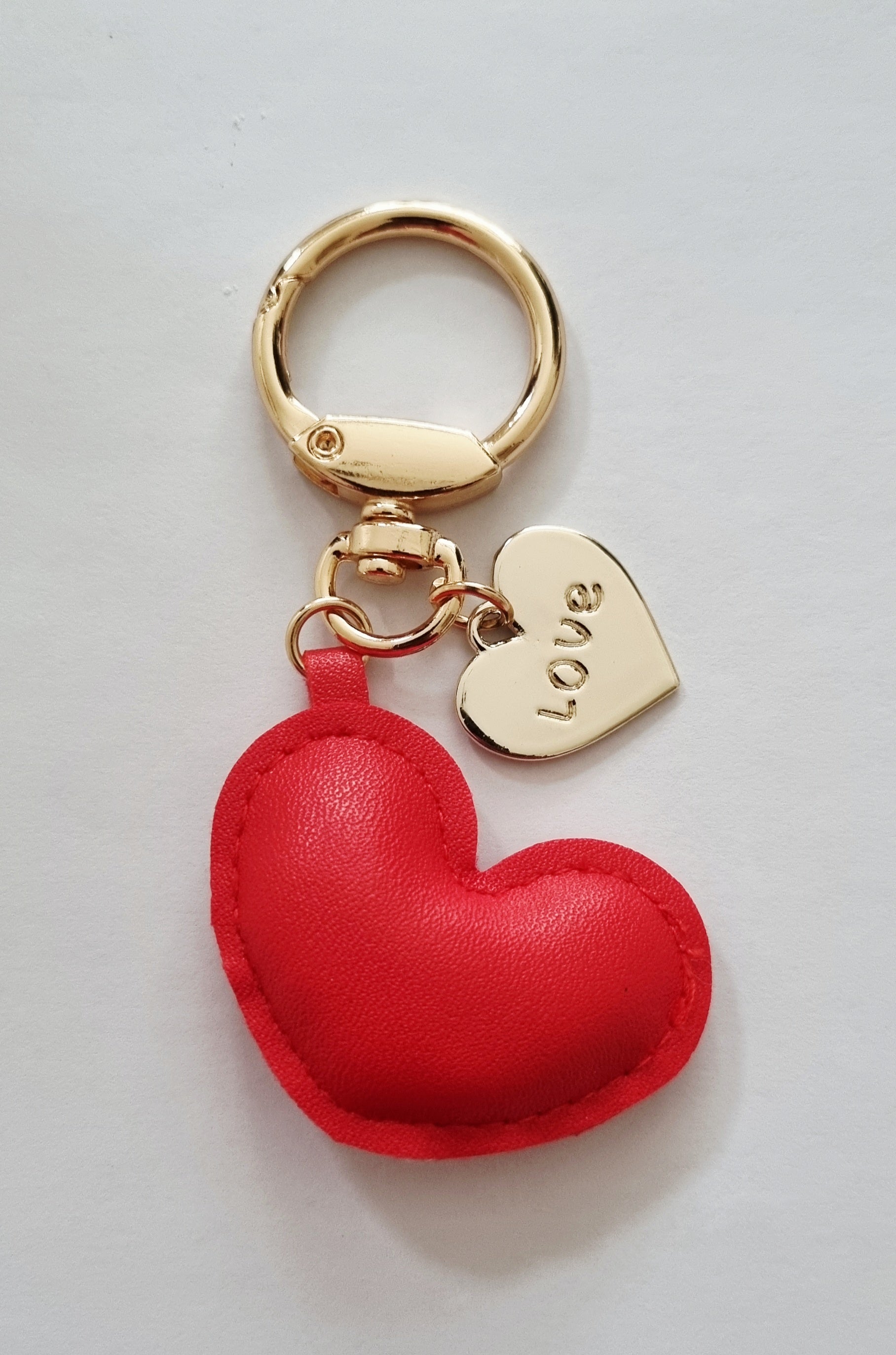 Red heart-shaped keychain with a gold tag on a light white background. Perfect for teenager, adults and kids for backpacks, handbags and keys