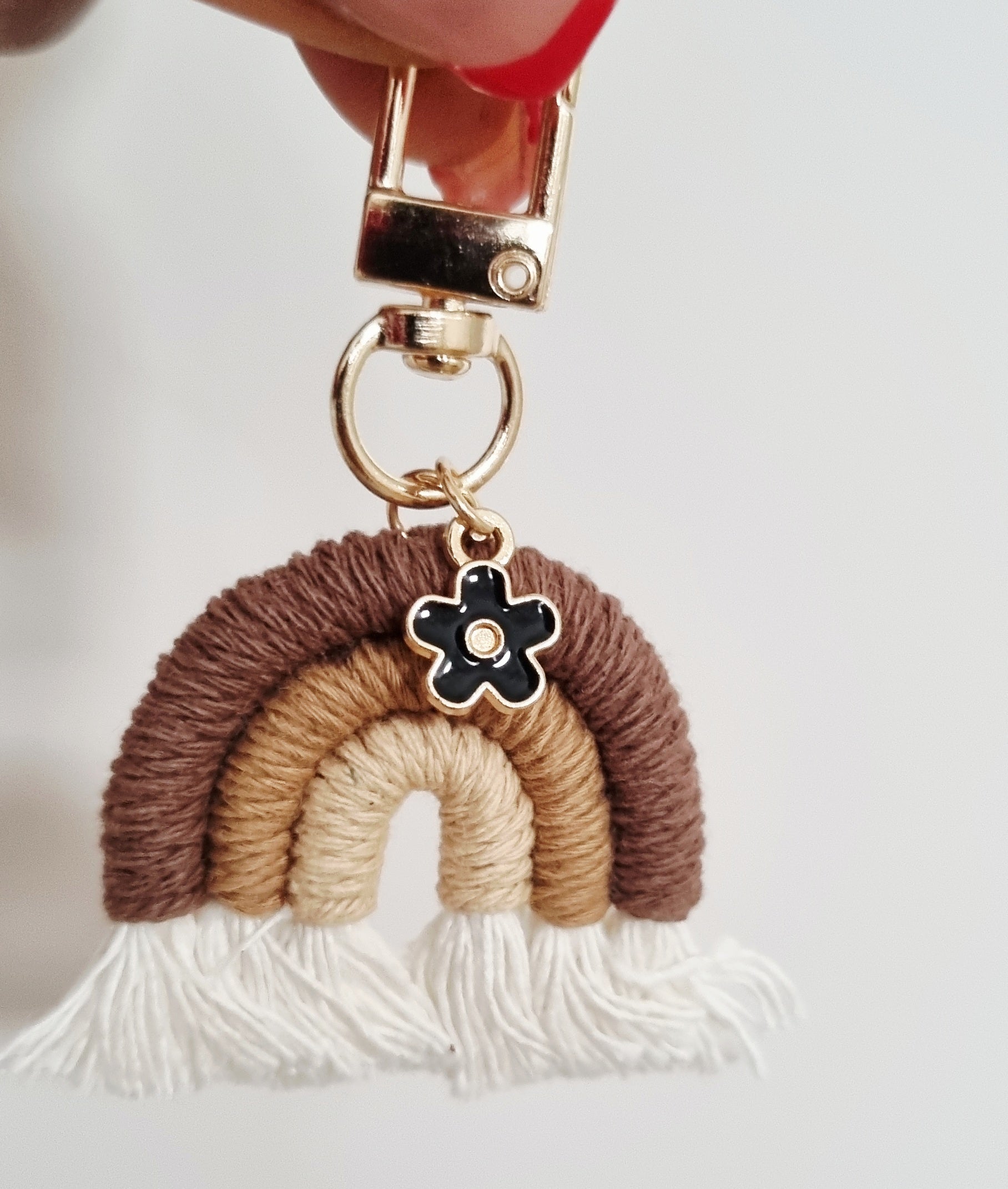 Keychain with rainbow design and flower charm held by a hand against a white background