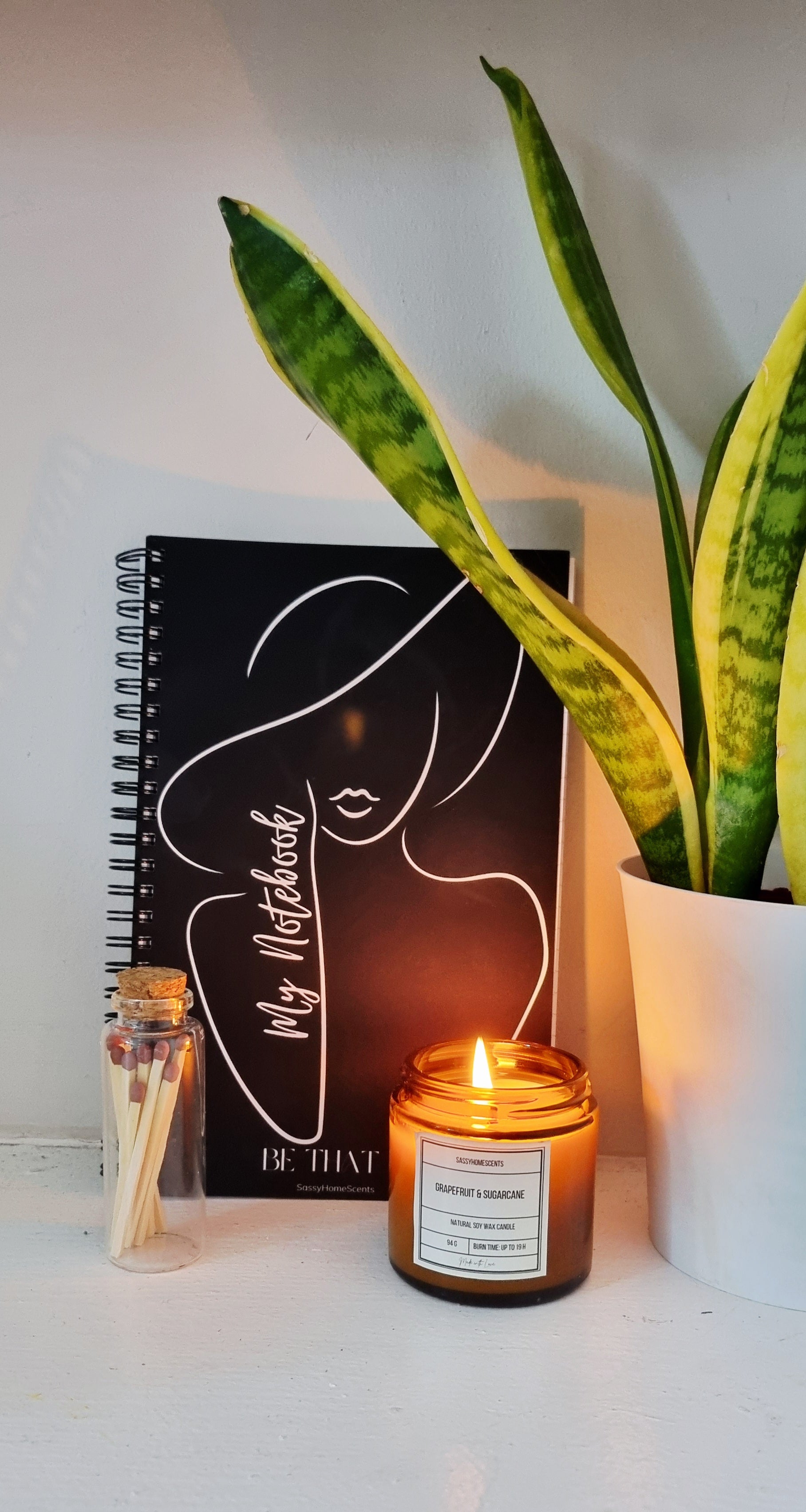 Candle, notebook, and plant on a white surface. Perfect for gifting, shop now
