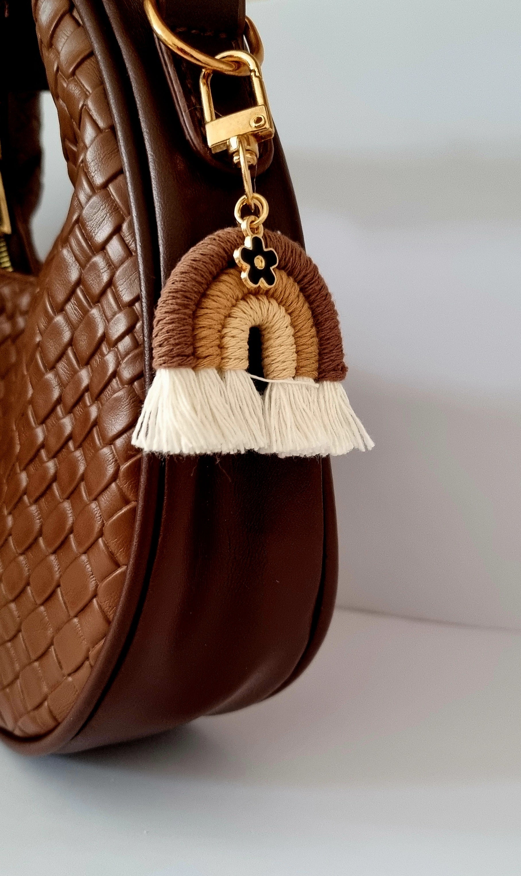 Decorative rainbow keychain with tassels attached to a brown textured bag.